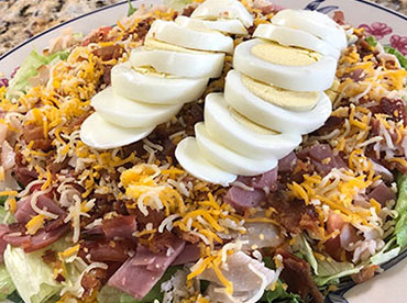 Chef's salad with lettuce, sliced boiled eggs, shredded cheese and ham served on a white plate