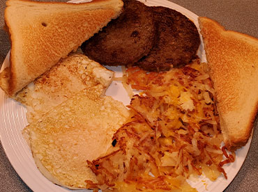 Hearty, country breakfast with eggs, sausage patties, hash browns and toast served on a white plate