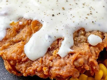 Country fried steak served with cream gravy on top with a side of corn kernels on a gray plate