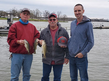 Three men standing on the bank of Lake Fork holding fish and smiling