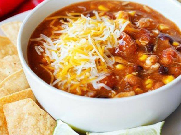 White bowl of chili with corn, black beans and cheese with tortilla chips served on a white plate
