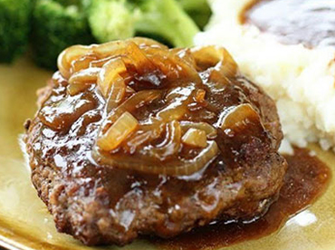 Hamburger steak topped with grilled onions and brown gravy with a side of masked potatoes and broccoli