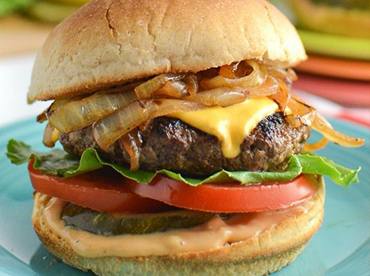 Delicious-looking cheeseburger with grilled onions, lettuce, tomato, pickle on a toasted bun served on a dark teal plate