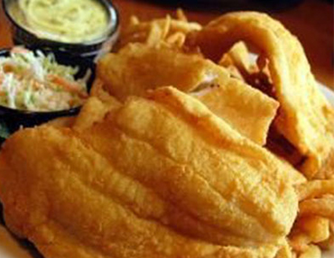 Fried, golden-brown catfish filets with french fried, coleslaw and tartar sauce served on a white plate 